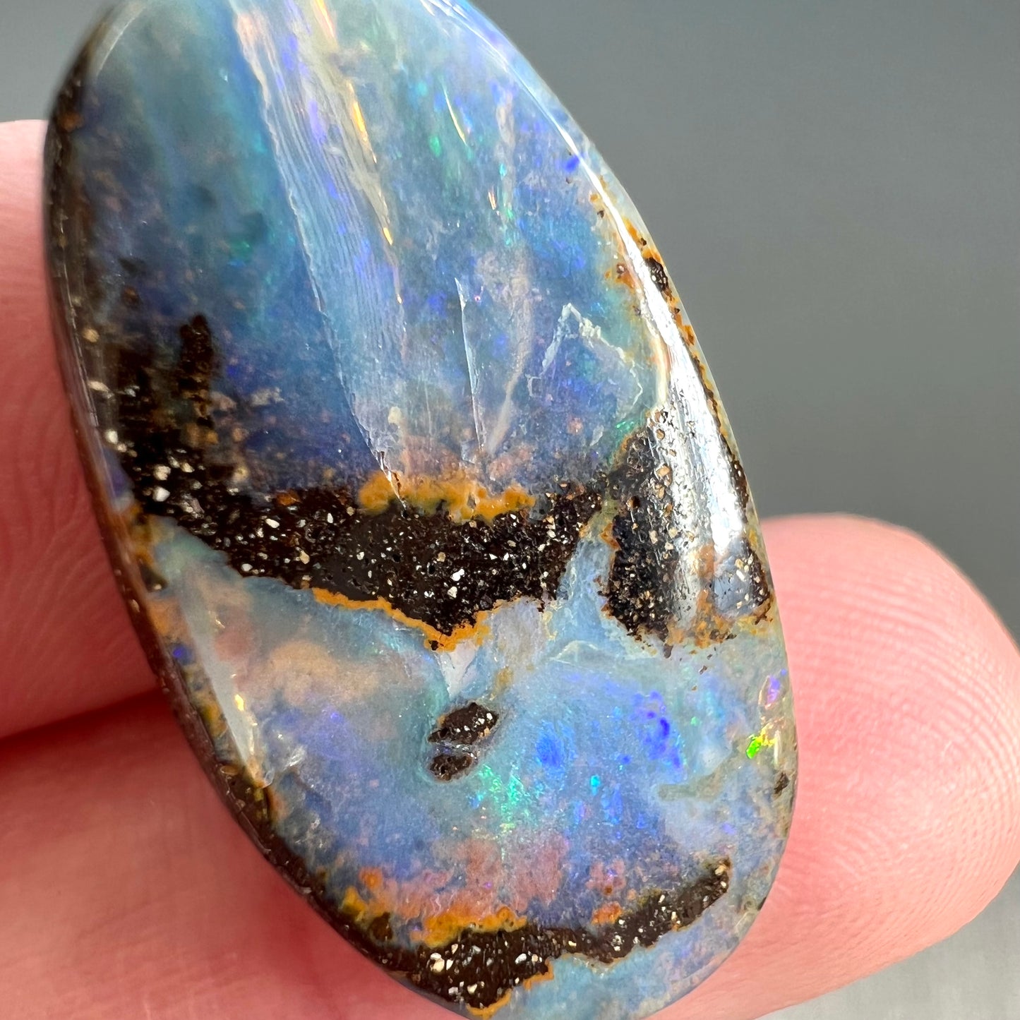 A loose, oval cabochon cut boulder opal stone from Queensland, Australia.