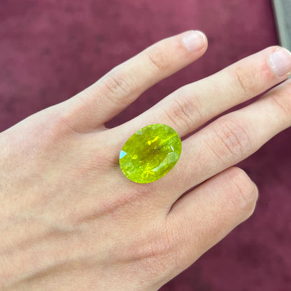 A loose, faceted oval cut green tourmaline stone.  The color is an almost neon yellow-green.