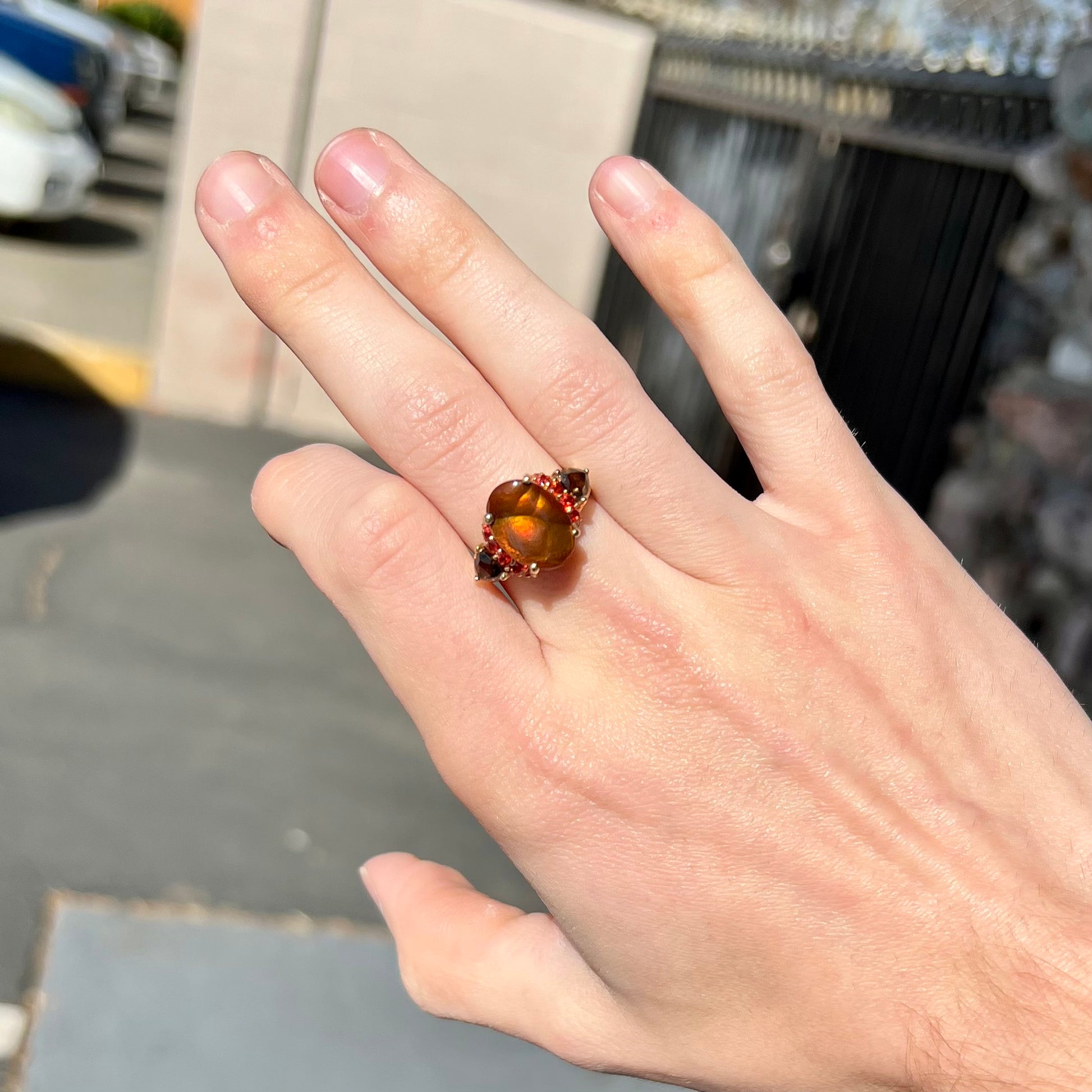 A ladies yellow gold fire agate ring set with trillion cut smoky quartz and round cut red-orange garnet accents.  The fire agate displays green and red.