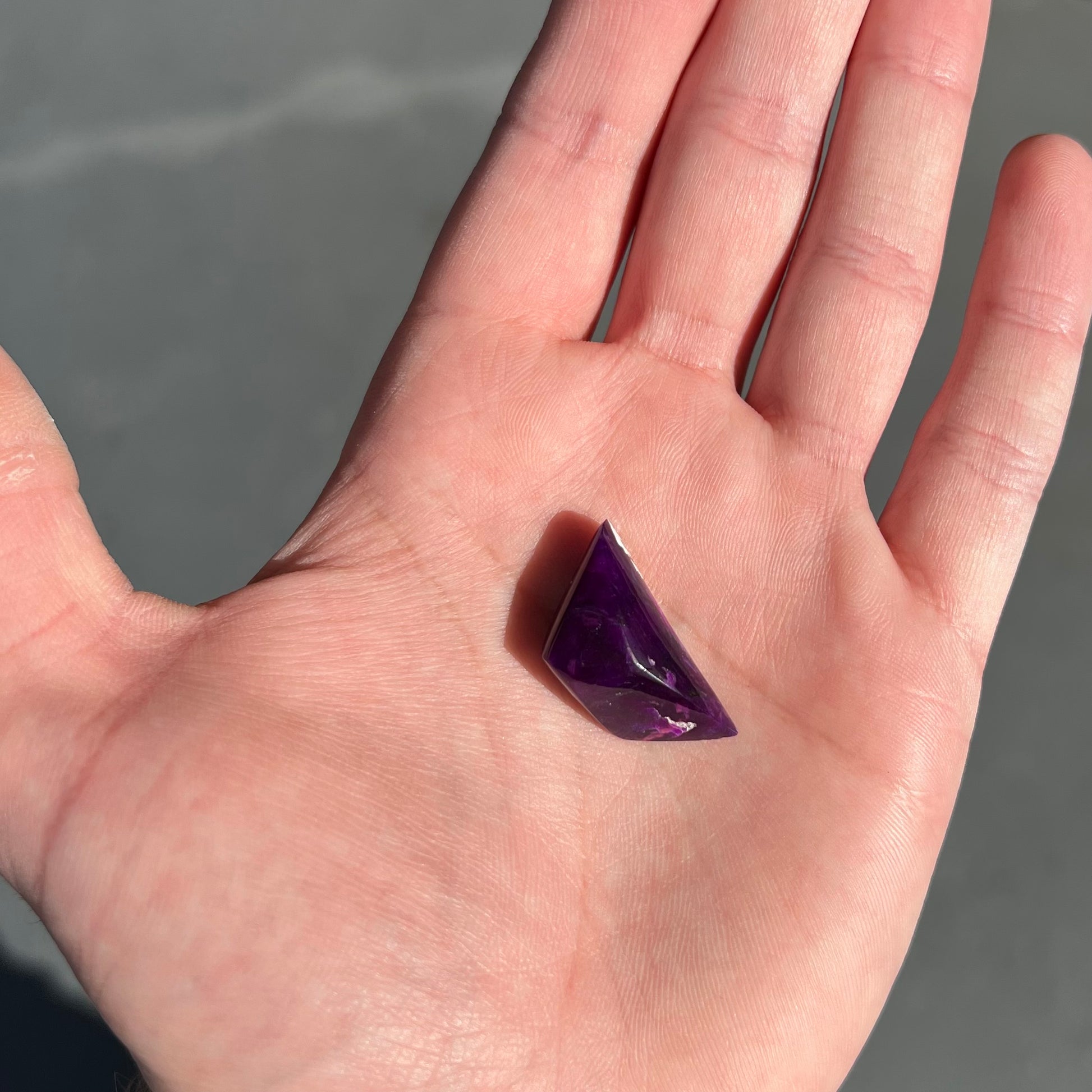 A freeform cabochon cut piece of dark purple sugilite.