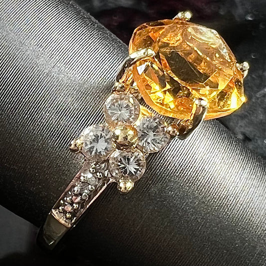 A cushion cut citrine set in a yellow gold ring with four round white sapphires and two diamonds on each side.