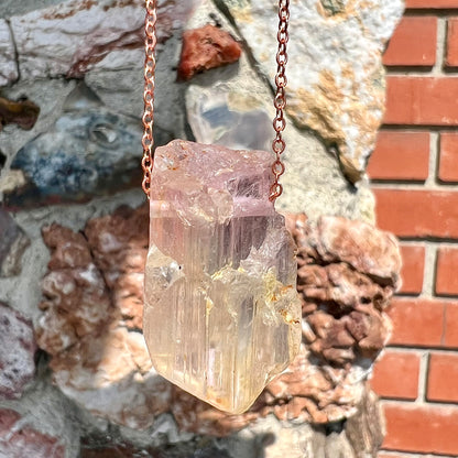 A drilled bicolor spodumene crystal hanging on a copper cable chain.  The crystal is pink and yellow, or kunzite and triphane respectively.