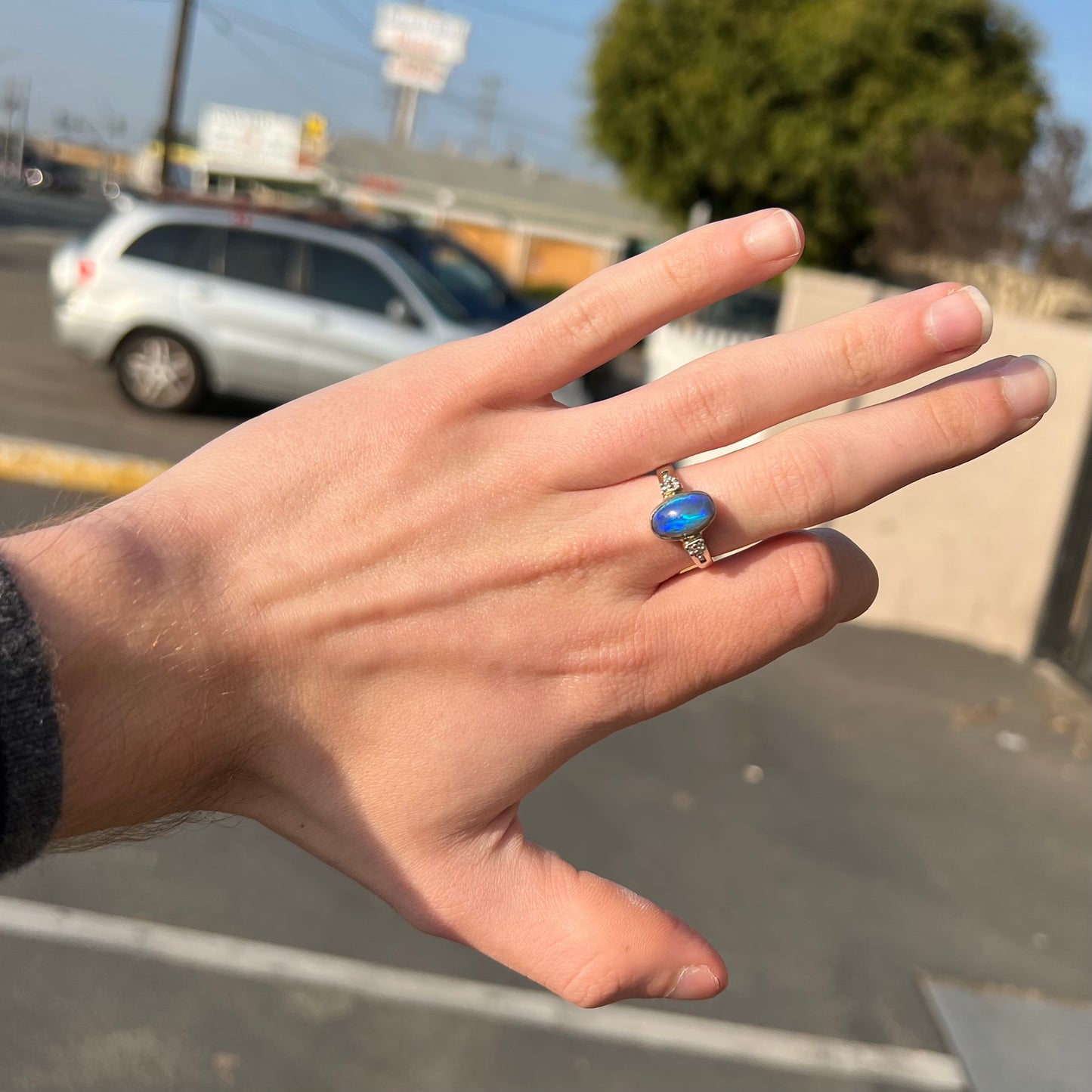 A white gold ring set with a Lightning Ridge black opal and diamond accents.  The opal displays a cat's eye pattern.