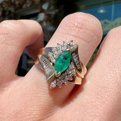 A yellow gold marquise cut emerald and diamond ring.  The diamonds are prong set round cuts and channel set baguette cuts.