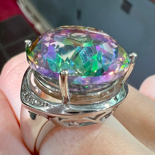 A large, round cut pink and green mystic topaz set in a sterling silver ring with white topaz accent stones.