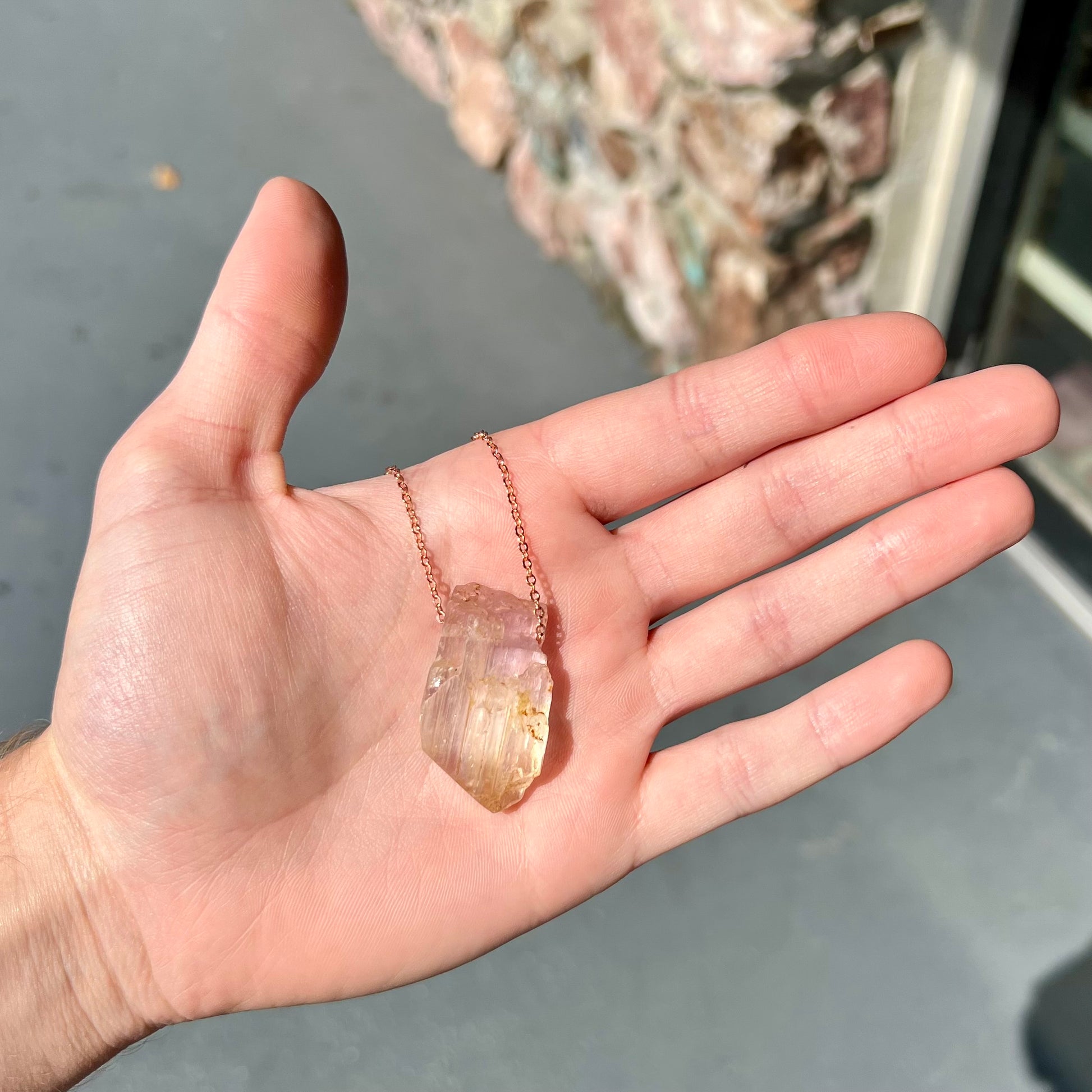 A drilled bicolor spodumene crystal hanging on a copper cable chain.  The crystal is pink and yellow, or kunzite and triphane respectively.