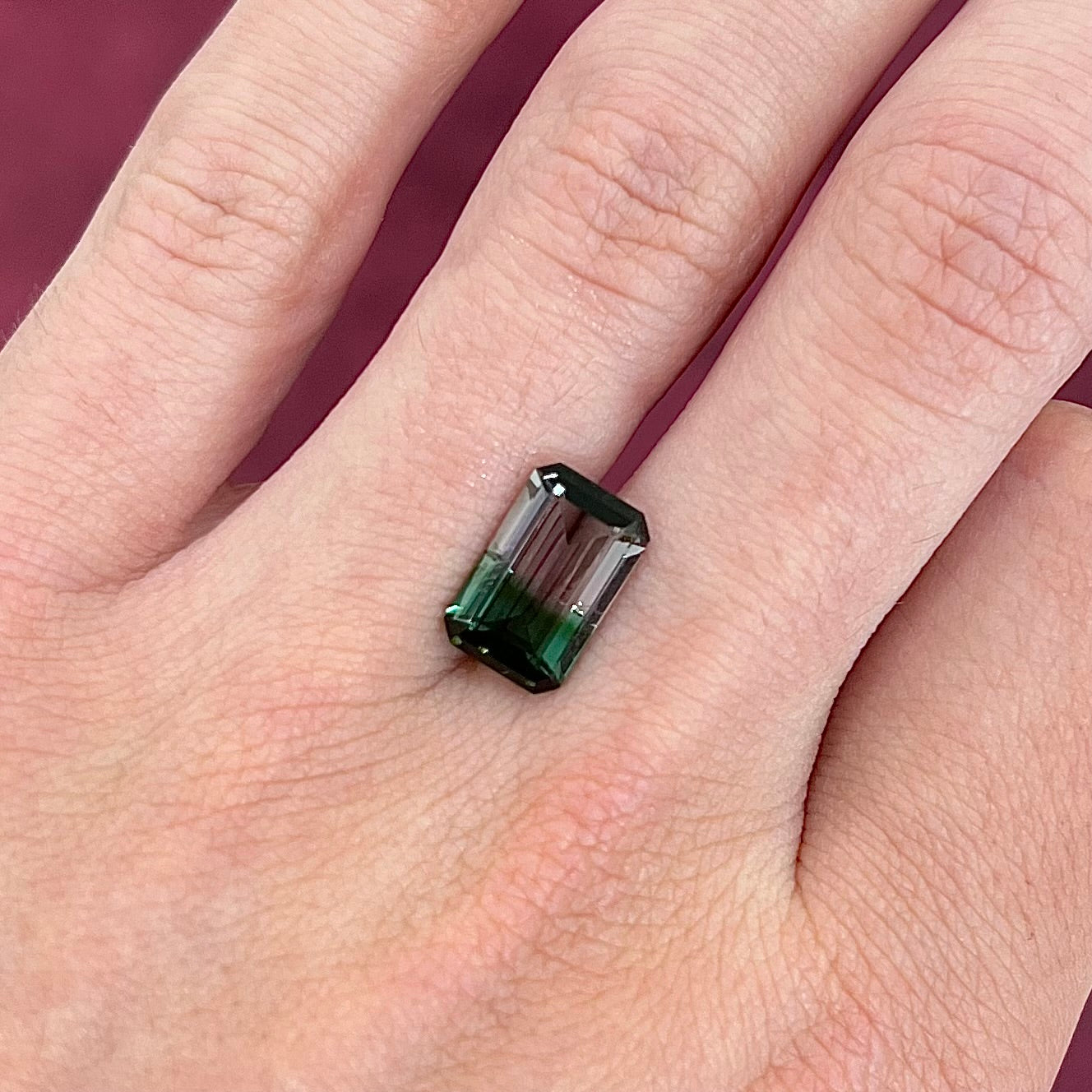 A loose, emerald cut bicolor tourmaline stone with a natural color separation of bluish green and light puce.