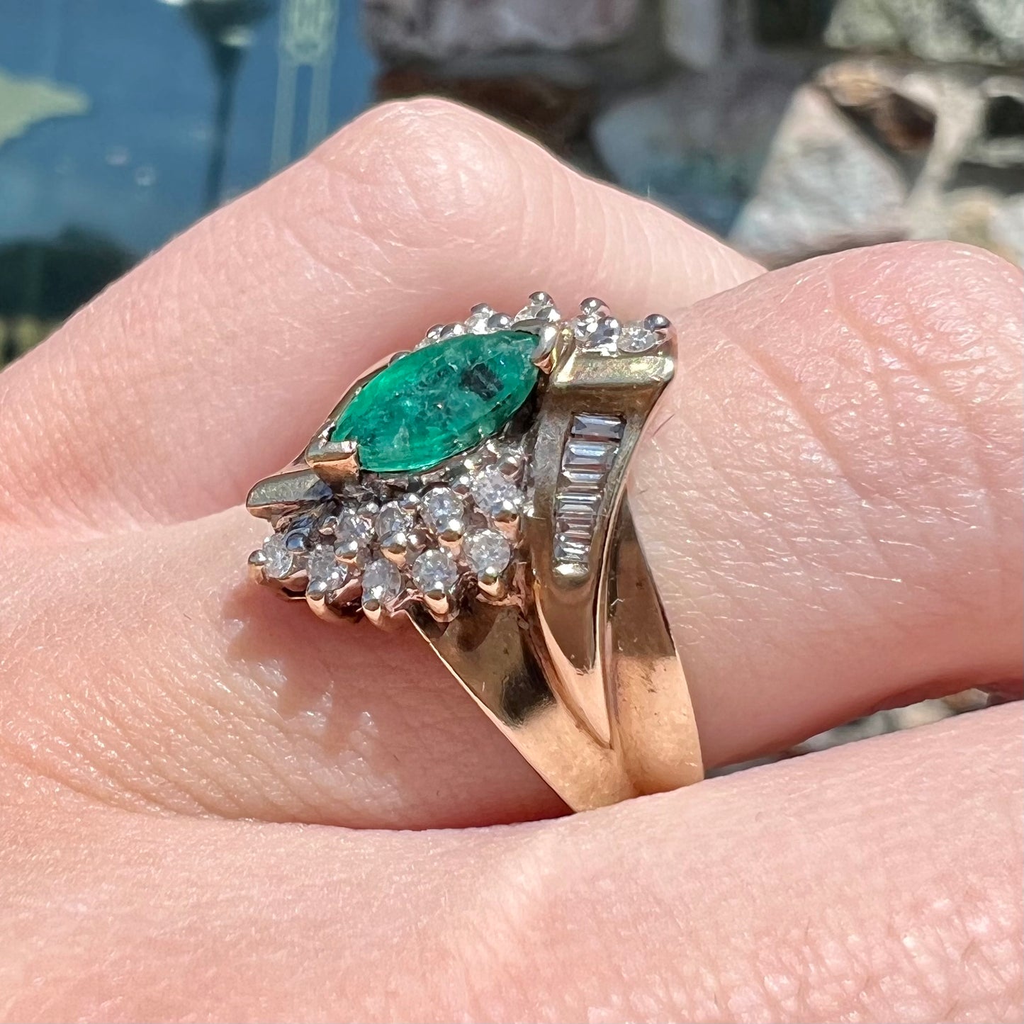 A yellow gold marquise cut emerald and diamond ring.  The diamonds are prong set round cuts and channel set baguette cuts.