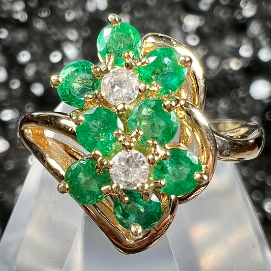 A yellow gold ring set with round cut emerald and diamonds that form the shape of two flowers.