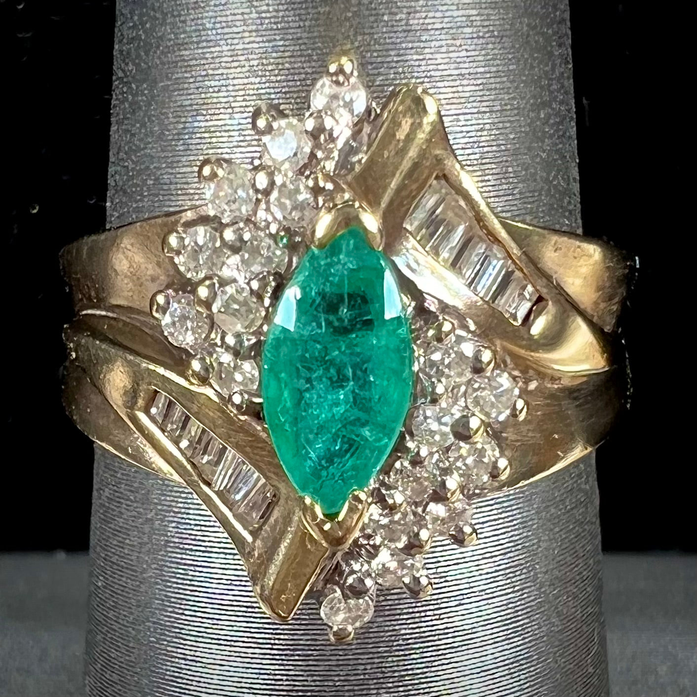 A yellow gold marquise cut emerald and diamond ring.  The diamonds are prong set round cuts and channel set baguette cuts.