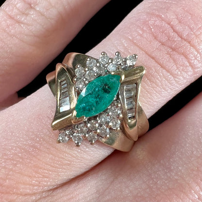 A yellow gold marquise cut emerald and diamond ring.  The diamonds are prong set round cuts and channel set baguette cuts.