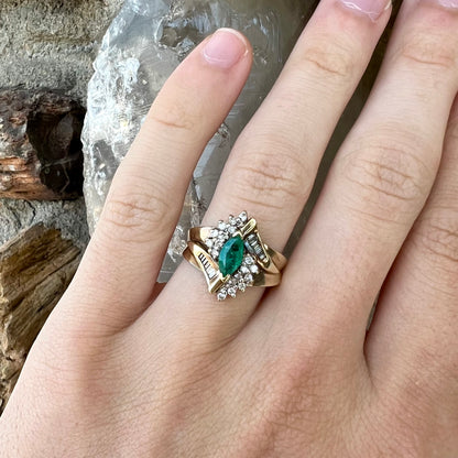 A yellow gold marquise cut emerald and diamond ring.  The diamonds are prong set round cuts and channel set baguette cuts.