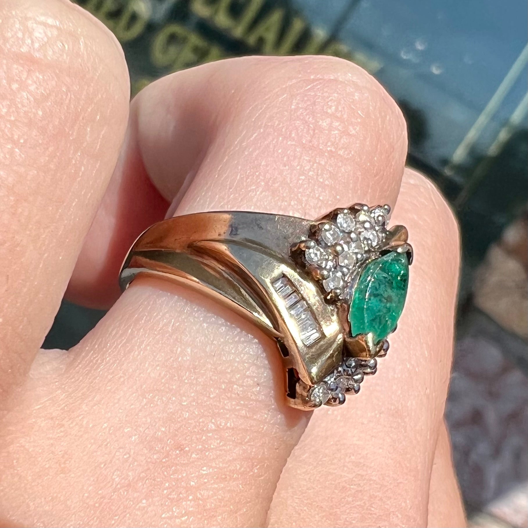 A yellow gold marquise cut emerald and diamond ring.  The diamonds are prong set round cuts and channel set baguette cuts.