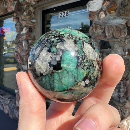 A gemstone sphere carved from a natural emerald crystal specimen, measuring 2.2 inches in diameter.