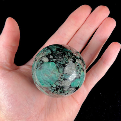 A gemstone sphere carved from a natural emerald crystal specimen, measuring 2.2 inches in diameter.