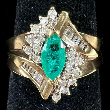 A yellow gold marquise cut emerald and diamond ring.  The diamonds are prong set round cuts and channel set baguette cuts.