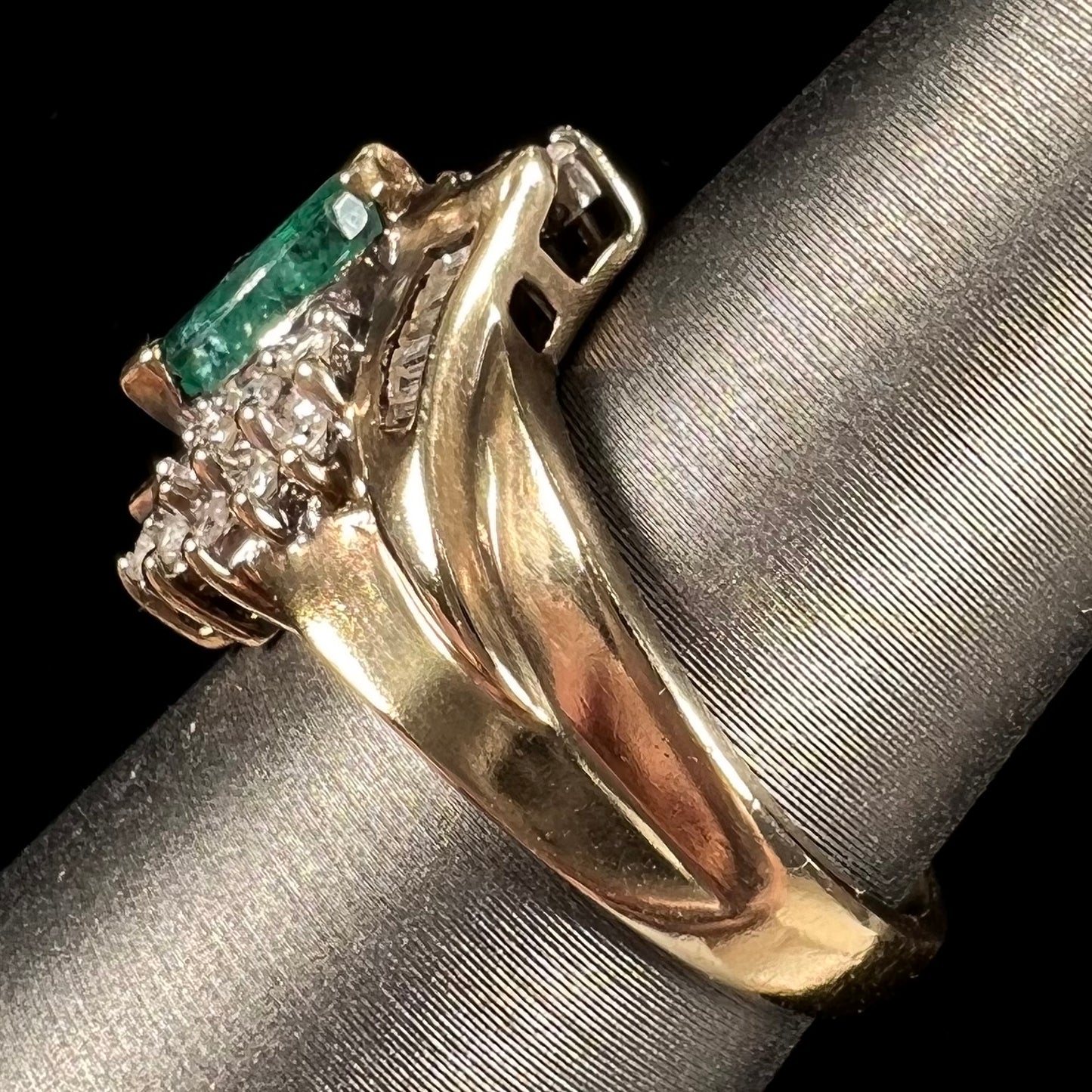 A yellow gold marquise cut emerald and diamond ring.  The diamonds are prong set round cuts and channel set baguette cuts.