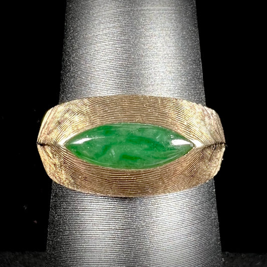 A textured yellow gold ring set with a marquise cabochon cut green jadeite stone.