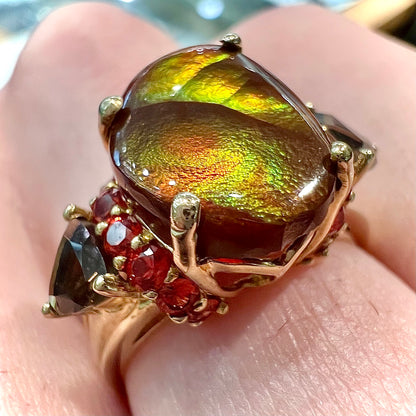 A ladies yellow gold fire agate ring set with trillion cut smoky quartz and round cut red-orange garnet accents.  The fire agate displays green and red.