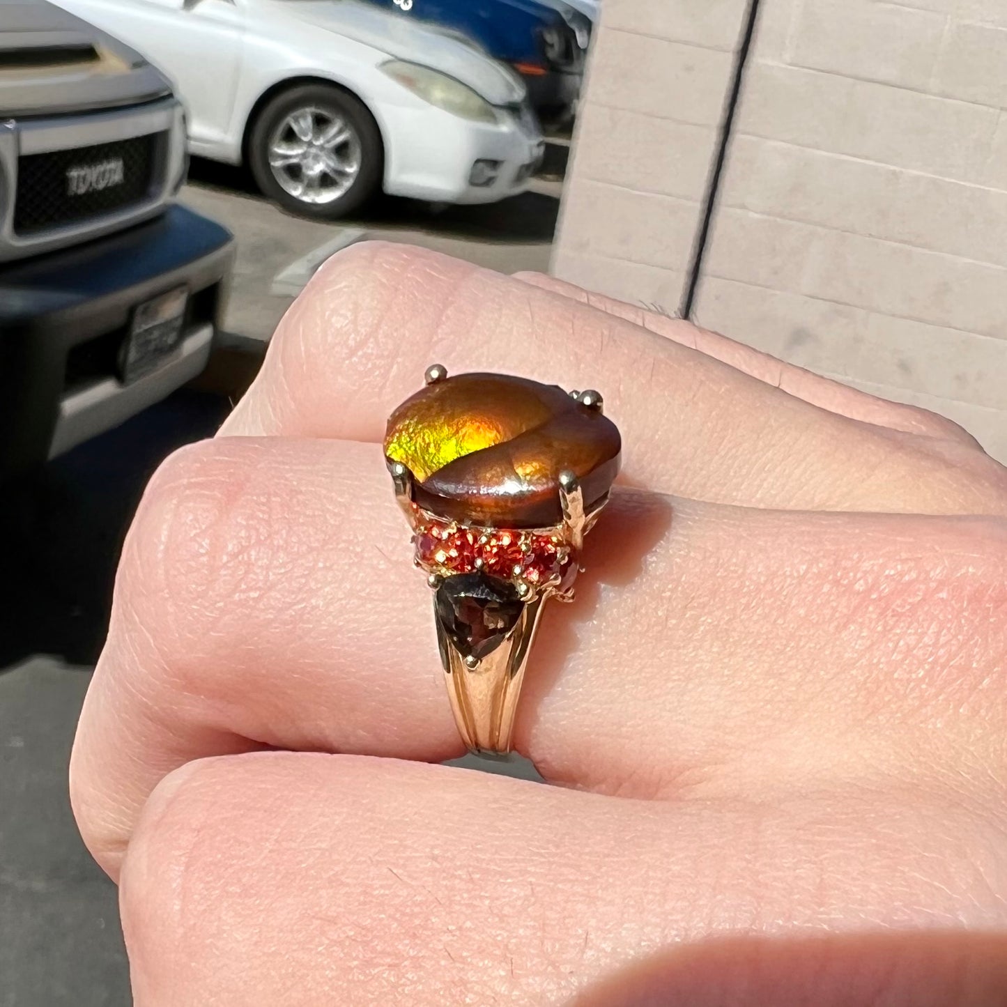 A ladies yellow gold fire agate ring set with trillion cut smoky quartz and round cut red-orange garnet accents.  The fire agate displays green and red.