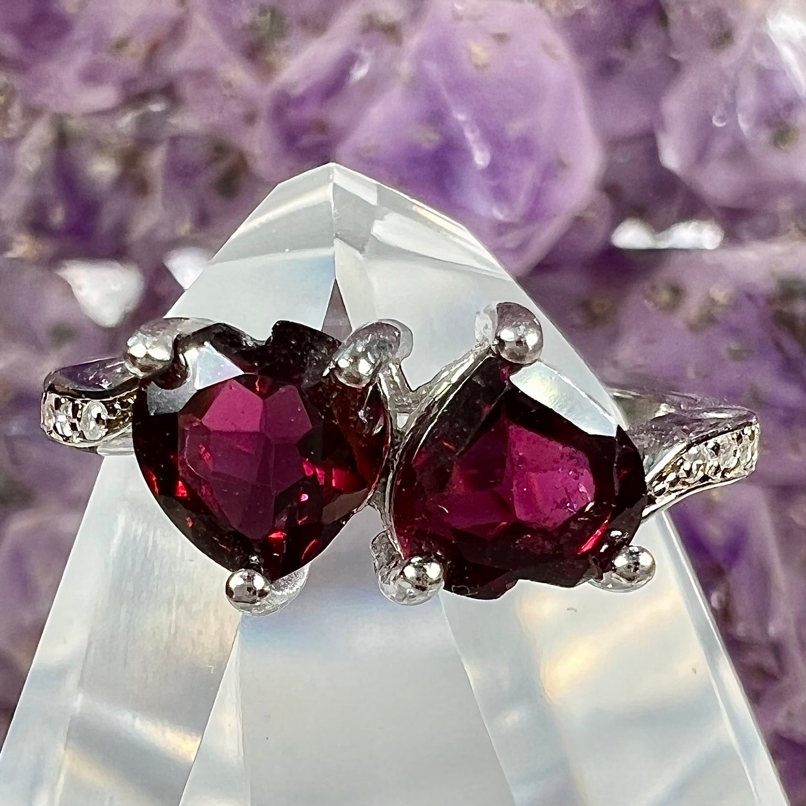 A sterling silver ring set with two faceted heart shape red almandine garnet stones.