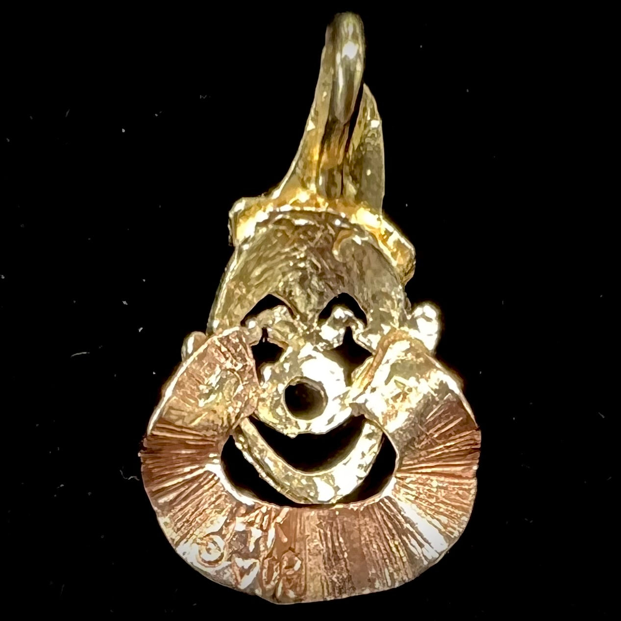 A small gold clown pendant charm.  The clown's face and hat are yellow gold, and his neck frills are rose gold.