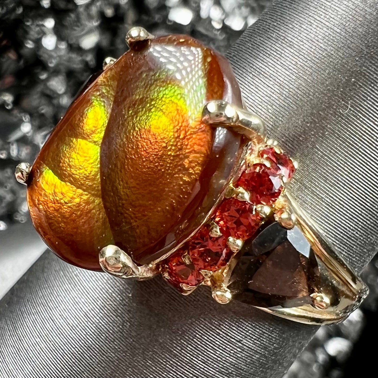 A ladies yellow gold fire agate ring set with trillion cut smoky quartz and round cut red-orange garnet accents.  The fire agate displays green and red.