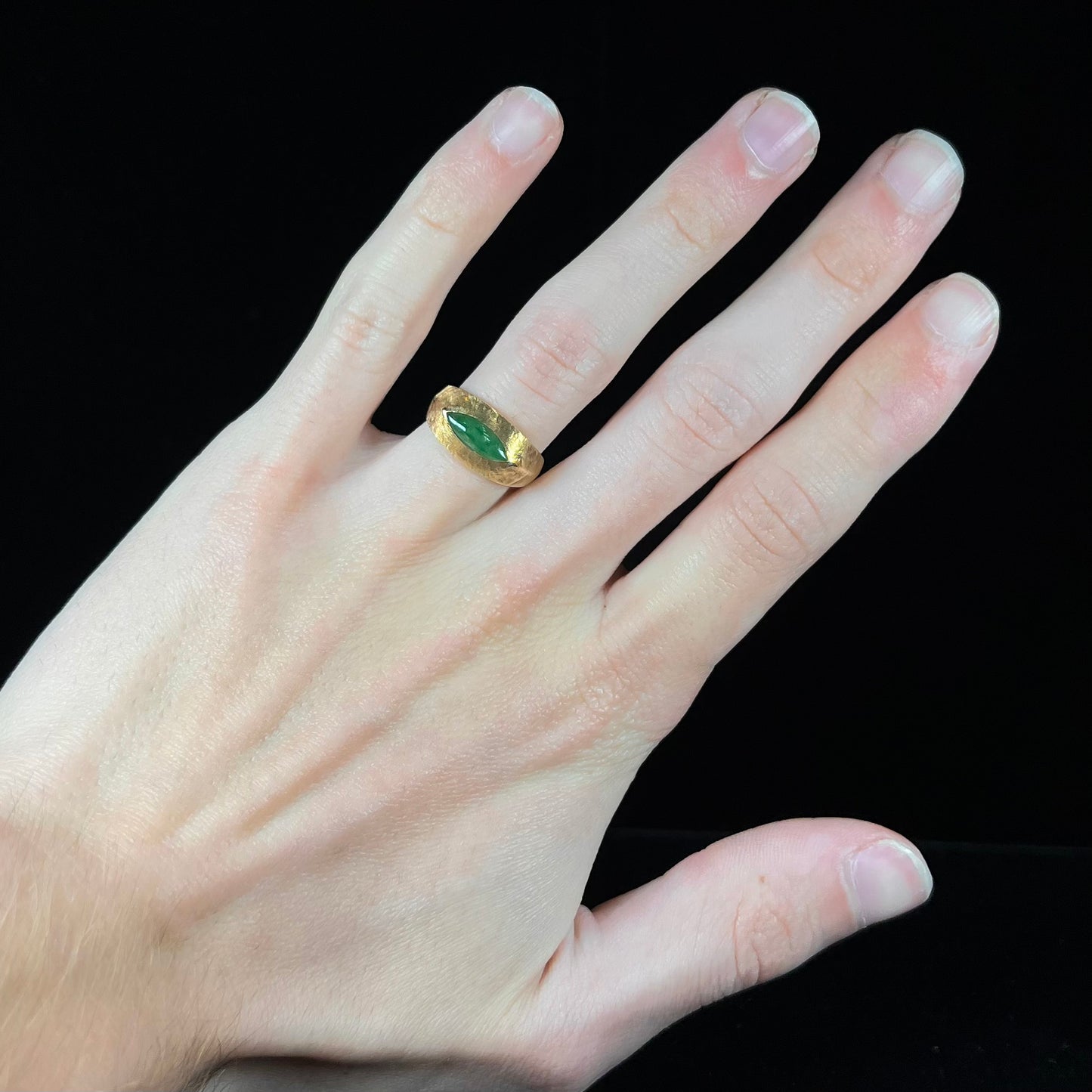 A textured yellow gold ring set with a marquise cabochon cut green jadeite stone.