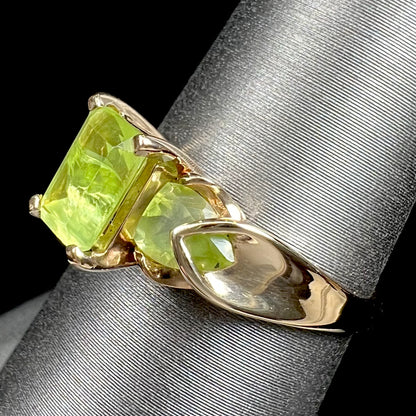 A ladies' three stone peridot ring in yellow gold.  The center stone is emerald cut, and the side stones are pear shaped.