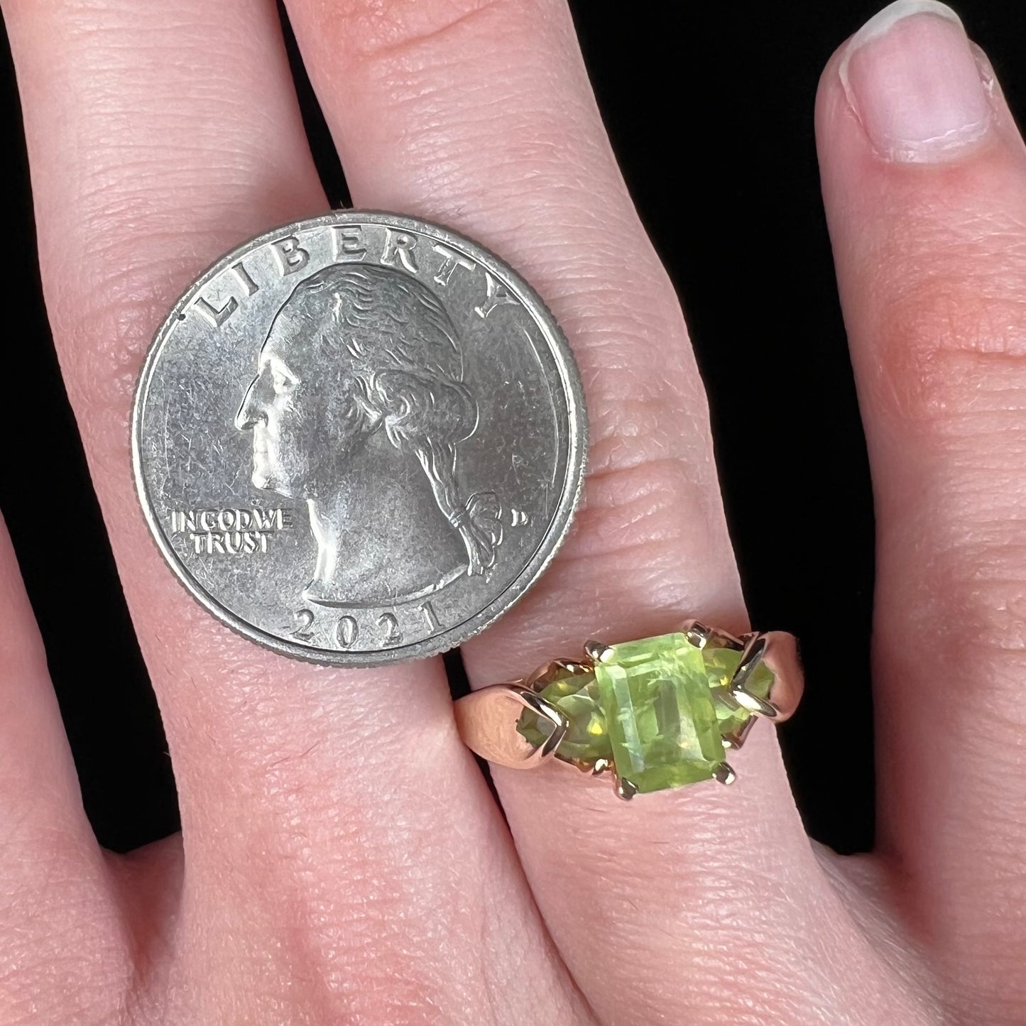 A ladies' three stone peridot ring in yellow gold.  The center stone is emerald cut, and the side stones are pear shaped.