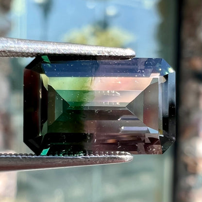 A loose, emerald cut bicolor tourmaline stone with a natural color separation of bluish green and light puce.