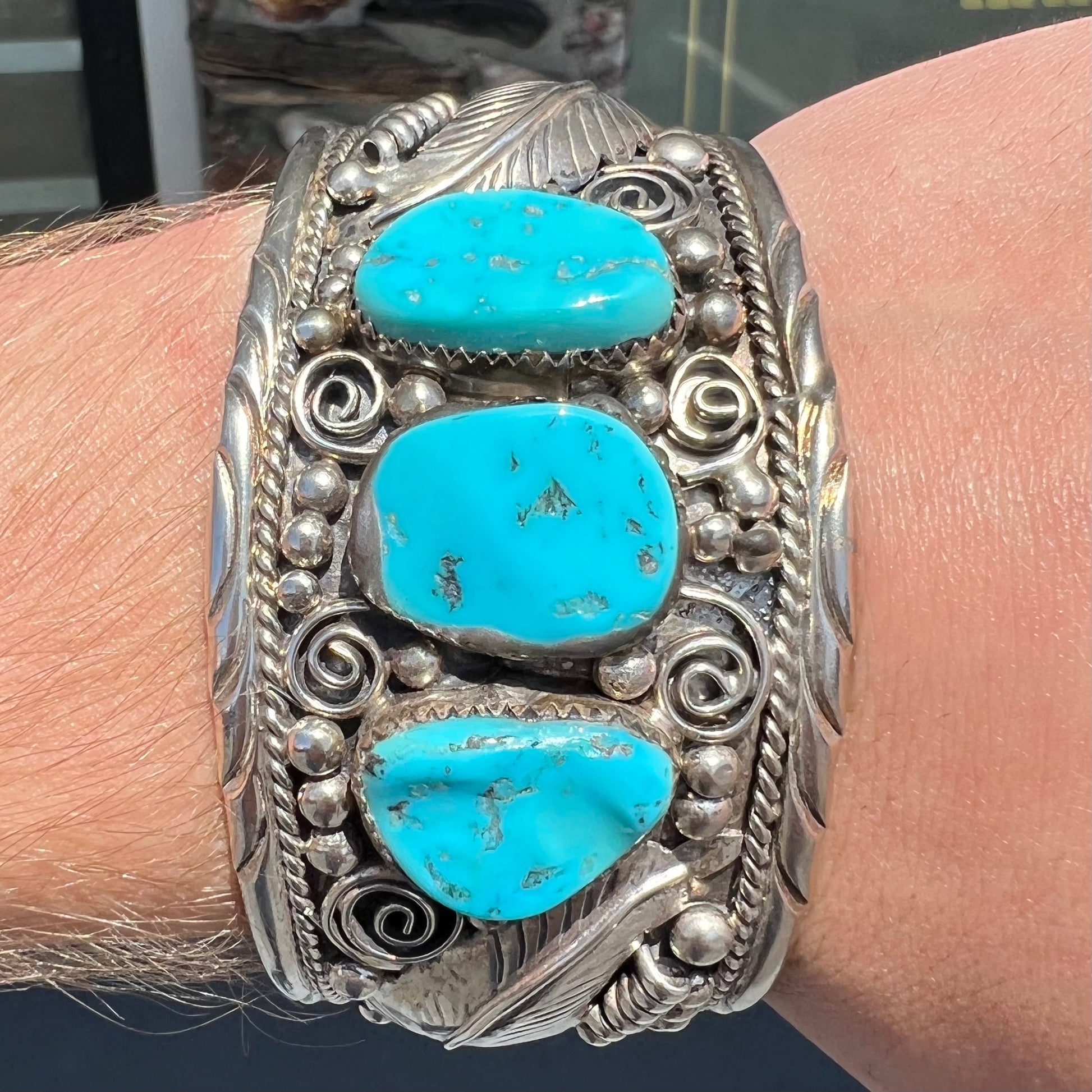 An ornate men's sterling silver turquoise cuff bracelet.  There are three turquoise stones set with silver feathers.