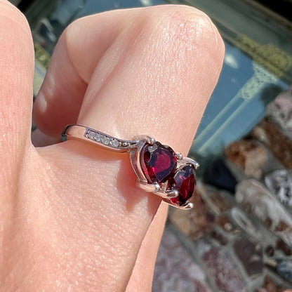 A sterling silver ring set with two faceted heart shape red almandine garnet stones.