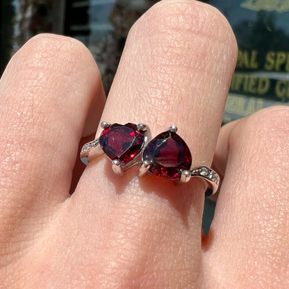 A sterling silver ring set with two faceted heart shape red almandine garnet stones.