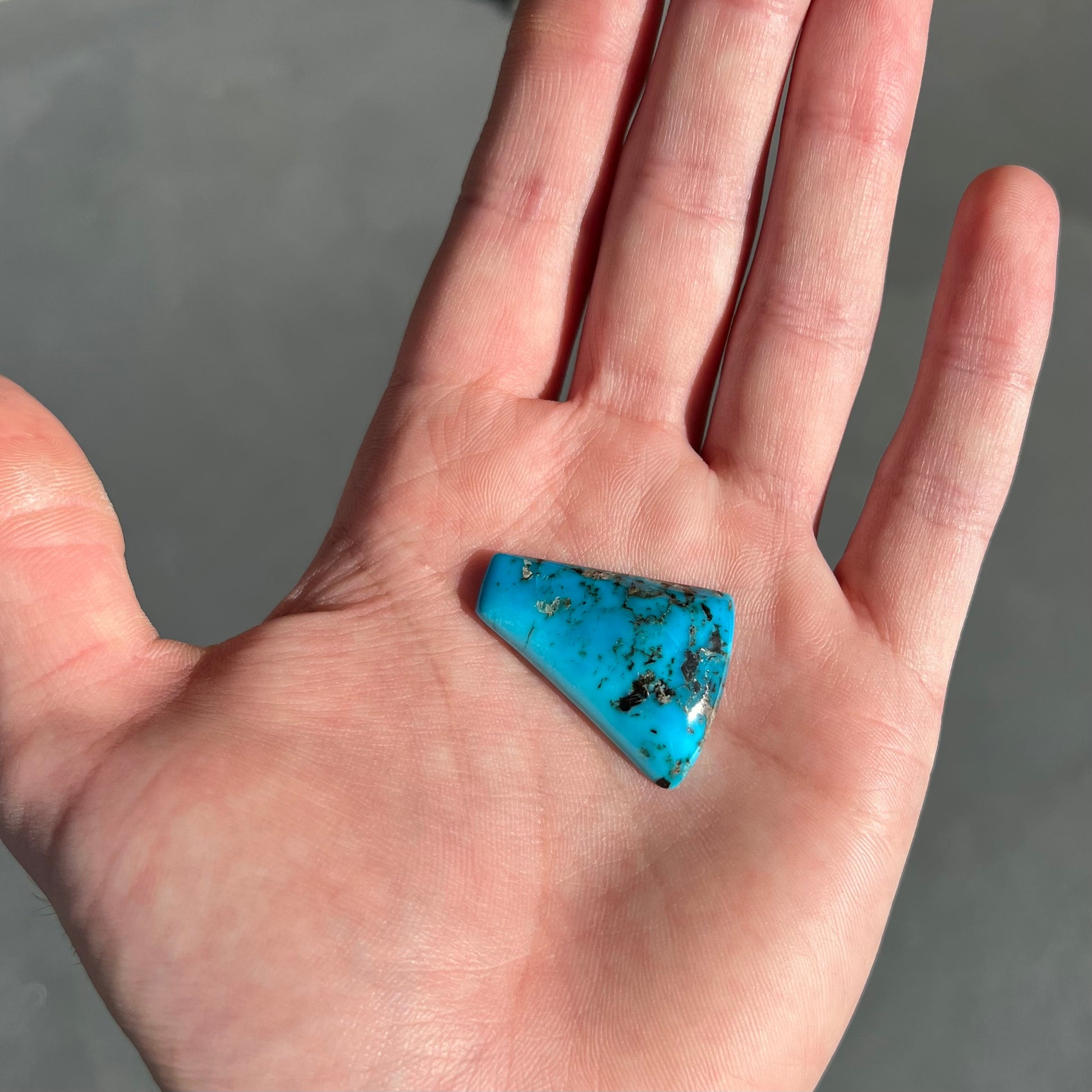 A loose, freeform triangle cabochon cut turquoise stone from the Sleeping Beauty Mine in Arizona.