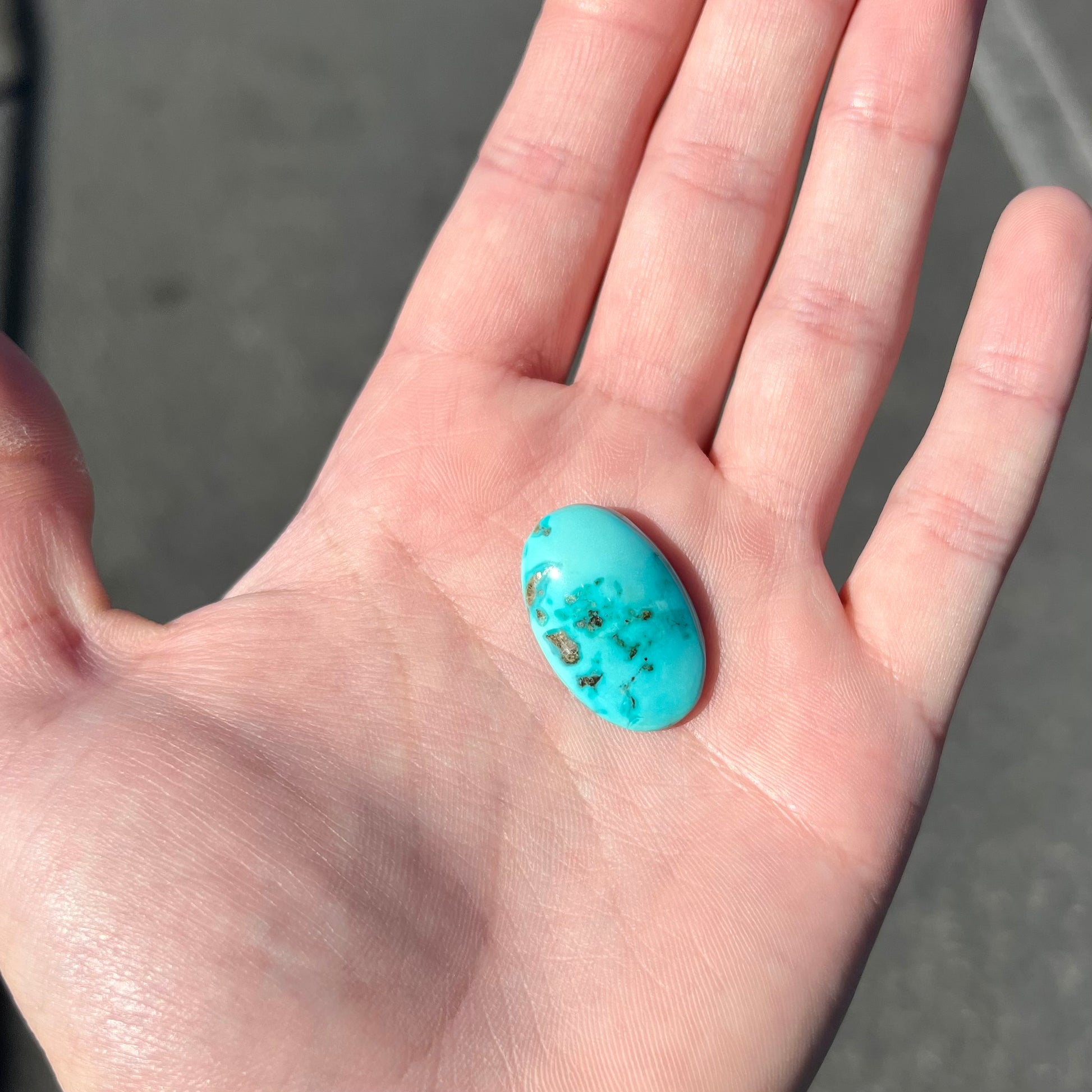 A loose, oval cut turquoise cabochon stone sitting in the palm of someone's hand.