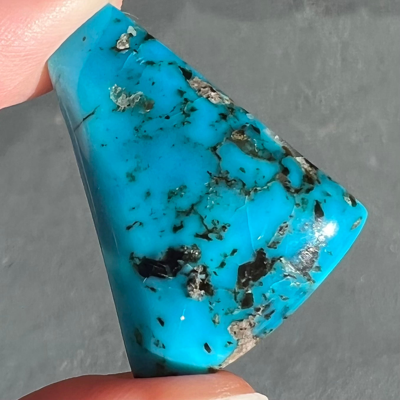 A loose, freeform triangle cabochon cut turquoise stone from the Sleeping Beauty Mine in Arizona.