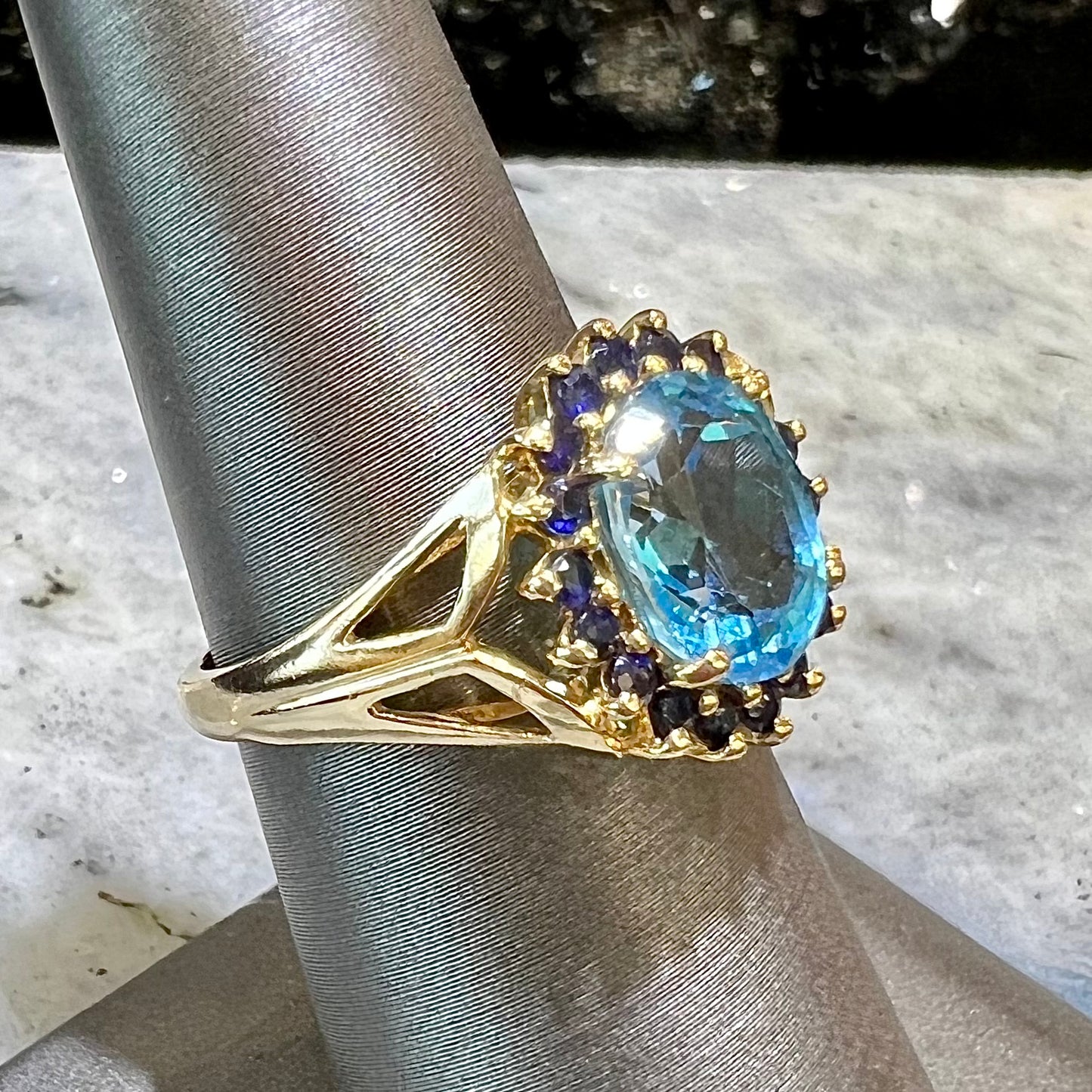 Yellow gold ring prong set with swiss blue topaz center stone and a halo of blue round blue sapphires.