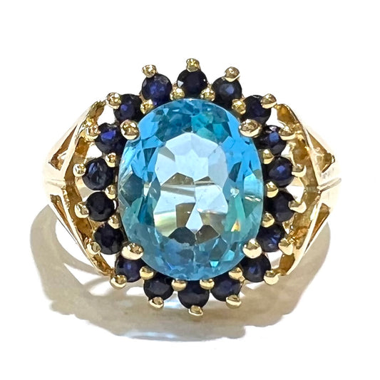 Yellow gold ring prong set with swiss blue topaz center stone and a halo of blue round blue sapphires.