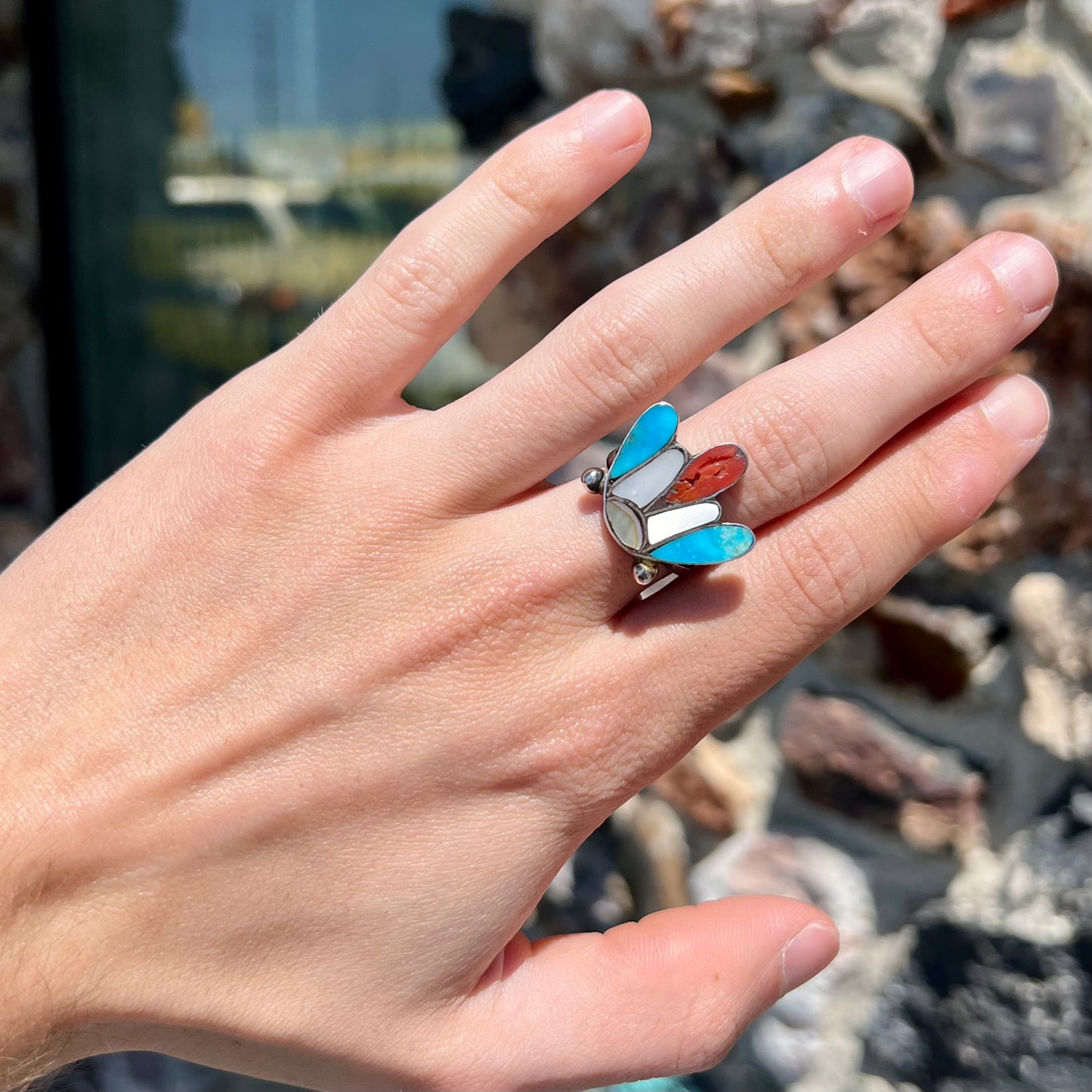 A turquoise, coral, and mother of pearl stone inlay ring made in the motif of a Zuni Indian headdress.