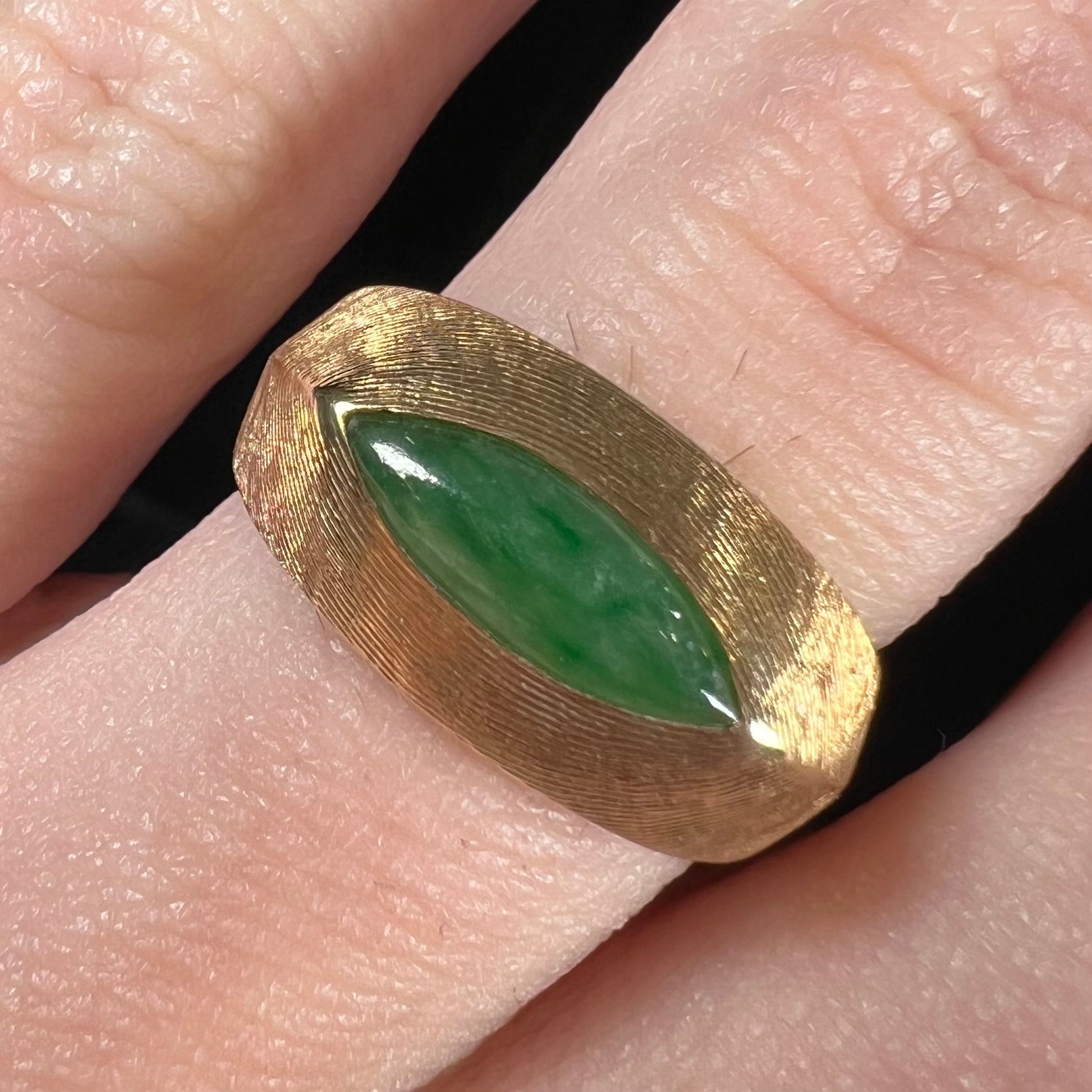 A textured yellow gold ring set with a marquise cabochon cut green jadeite stone.