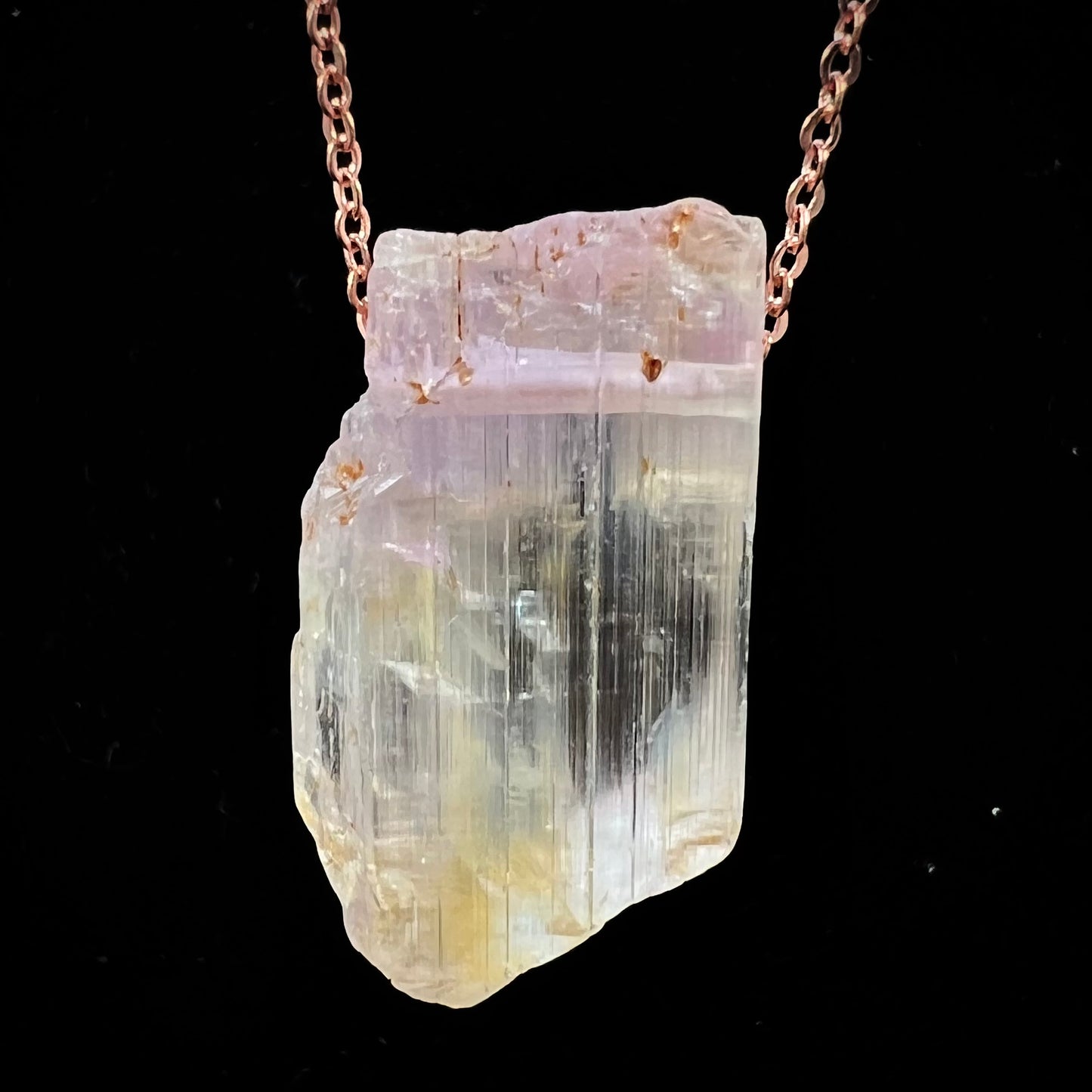 A drilled bicolor spodumene crystal hanging on a copper cable chain.  The crystal is pink and yellow, or kunzite and triphane respectively.