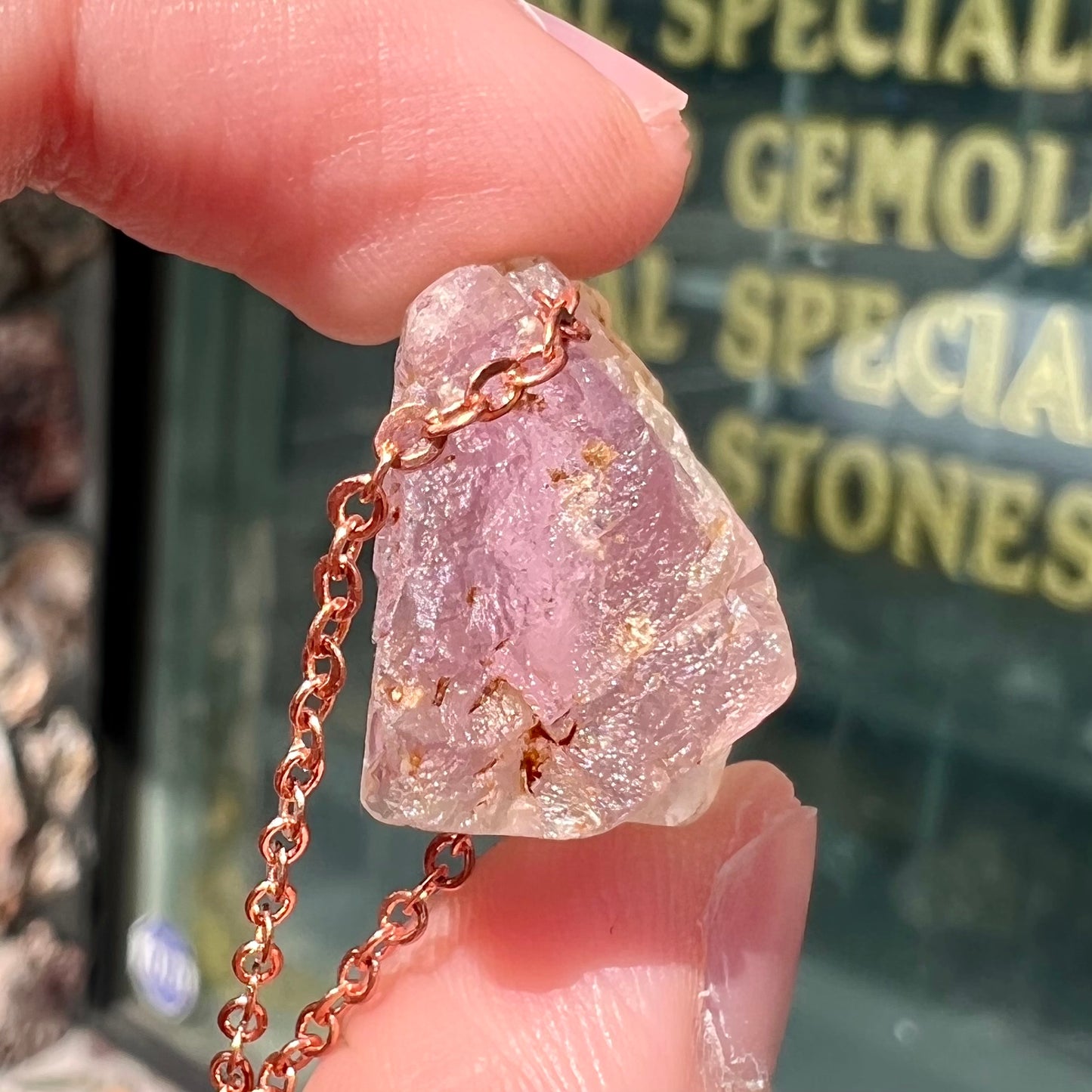 A drilled bicolor spodumene crystal hanging on a copper cable chain.  The crystal is pink and yellow, or kunzite and triphane respectively.