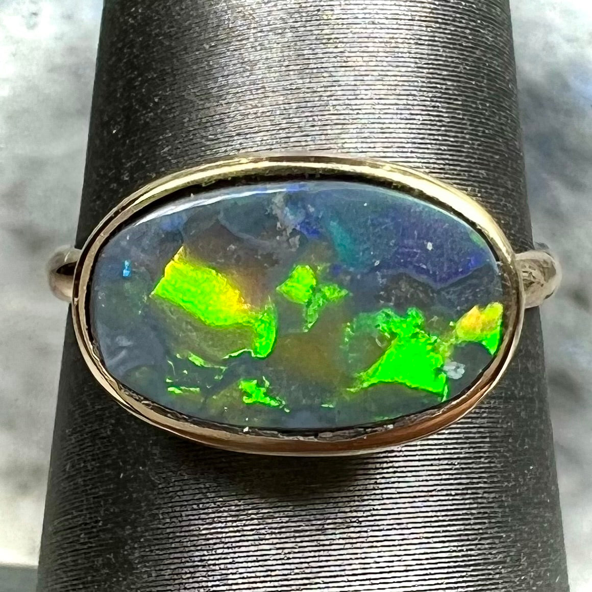 A handmade Lightning Ridge black opal solitaire ring in yellow gold.  Fire is green.