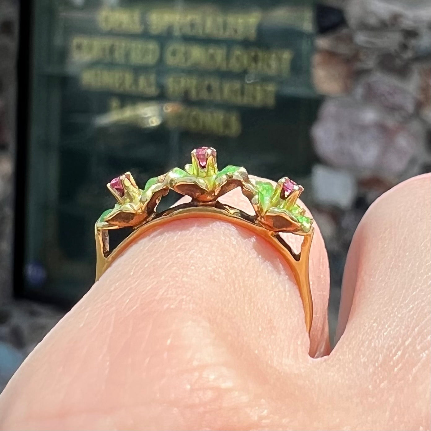 A gold ladies' ring in the motif of three flowers set with round ruby centers and green enameled petals.