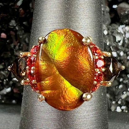 A ladies yellow gold fire agate ring set with trillion cut smoky quartz and round cut red-orange garnet accents.  The fire agate displays green and red.