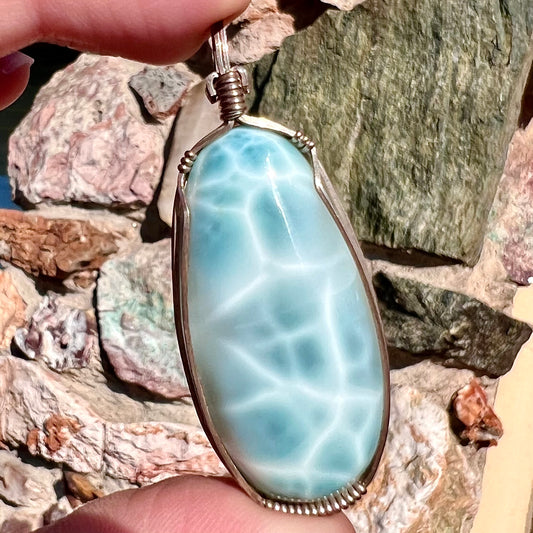 A large, oval cabochon cut blue larimar stone mounted in a sterling silver wire wrapped pendant.