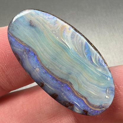 A loose, oval cabochon cut boulder opal stone from Queensland, Australia.