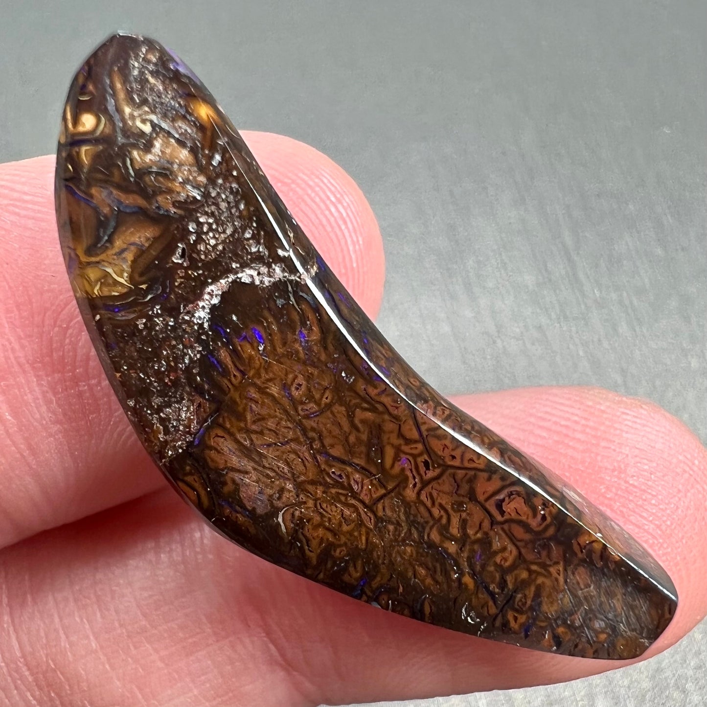 A loose boomerang shaped purple boulder opal stone from Quilpie, Australia.