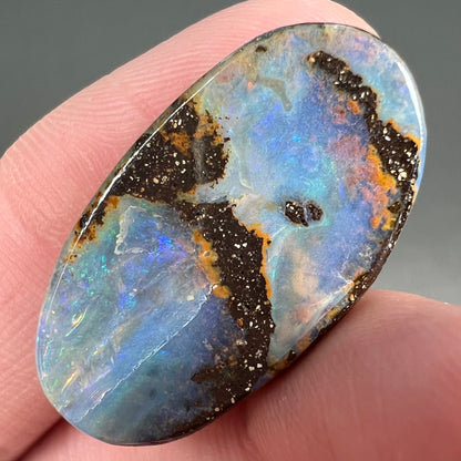 A loose, oval cabochon cut boulder opal stone from Queensland, Australia.